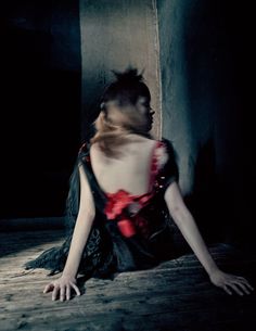 a woman sitting on the floor with her back turned to the camera, wearing a black and red corset