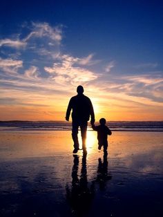 a man and child walking on the beach at sunset