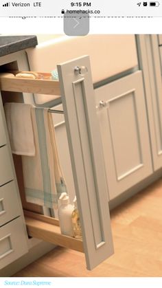 an open cabinet door in the middle of a kitchen with white cupboards and drawers