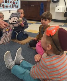 a group of children sitting on the floor playing with paper cut outs and scissors in front of them