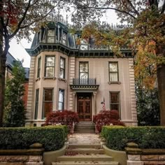 a large house with many trees and bushes around it's front entrance, on a cloudy day