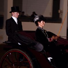 a man and woman riding in an old fashioned horse drawn buggy at night time