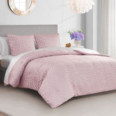 a bed with pink comforter and pillows in a room next to a mirror on the wall