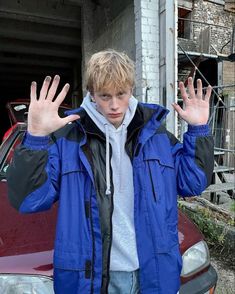 a young man standing in front of a red car with his hands up to the camera