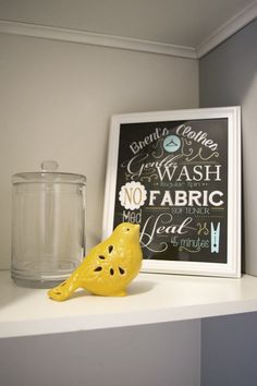 a yellow bird sitting on top of a white shelf next to a glass jar and sign