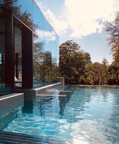 an empty swimming pool in front of a large glass wall with trees and bushes behind it