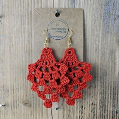 red crocheted earrings with gold tone hooks hang from a card on a wooden background