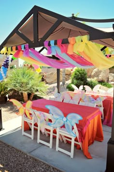 an outdoor dining area with tables and chairs covered in colorful cloths under a canopy