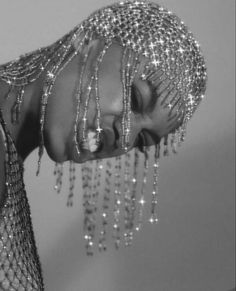 a woman with her face covered in chains and beads, looking down at the ground