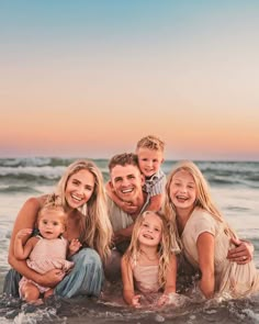 a family posing for a photo in the ocean at sunset with their two children and one adult