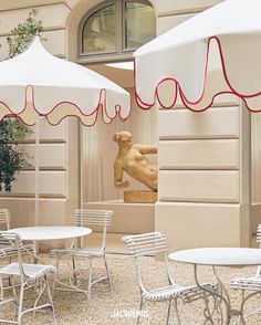 tables and chairs with white umbrellas in front of a building that has a statue on it