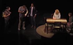 a group of people standing around a table on top of a dark stage with chairs