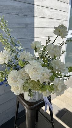 a vase with white flowers and greenery is sitting on a stool in front of a building