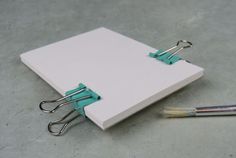 an open notebook with two binders attached to it and a paintbrush next to it