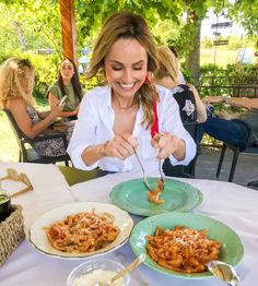 a woman is eating pasta at an outdoor table