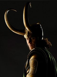 a man dressed as loki with horns on his head and caped shoulders, standing in front of a dark background