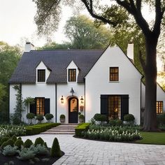 a white house with black shutters and trees in the front yard at sunset or dawn