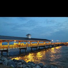 the pier is lit up at night with yellow lights on it's posts and benches