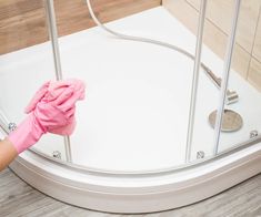 a person in pink gloves is cleaning a shower with a rag on the glass door