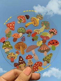 a hand holding up a clear sticker with lots of mushrooms on it in front of a blue sky