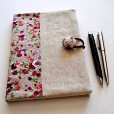 a notebook cover with flowers on it next to two pens