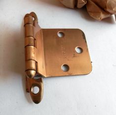 an old brass plated door hinge with holes in the middle and a piece of brown paper behind it