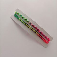 two colorful bracelets sitting on top of a white piece of paper next to each other