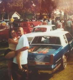 a man and woman standing in front of a car at a car show with other cars