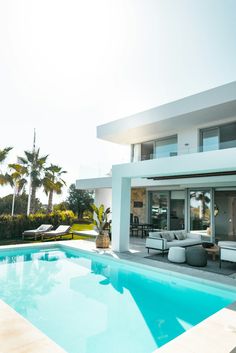 a large swimming pool in front of a modern house with lounge chairs and palm trees