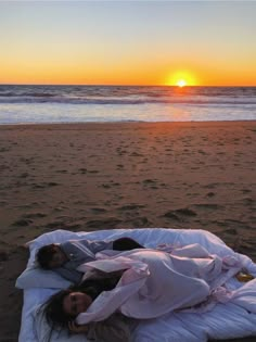 a woman laying on top of a bed under a blanket next to the ocean at sunset