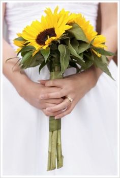 a bride holding a bouquet of sunflowers in her hands