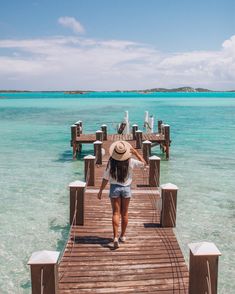 a woman walking across a wooden pier towards the ocean with clear blue water in the background