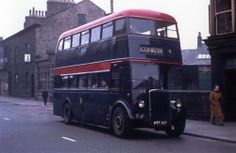 a double decker bus driving down a street next to tall buildings and people standing on the sidewalk