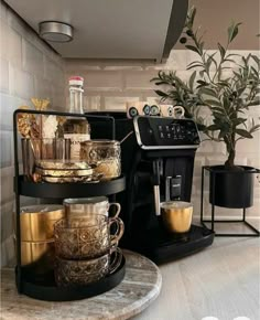 there is a coffee maker on the counter with cups in front of it and a potted plant next to it