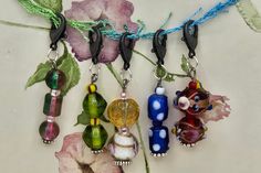 four glass bead charms hanging from a cord with flowers in the background on a white surface