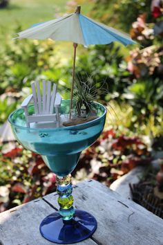 a blue cocktail with an umbrella and chair in the drink glass is sitting on a table outside