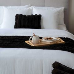 a tray with food on top of a bed next to a cup and saucer