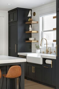 a kitchen with black cabinets, white counter tops and wooden stools in front of the sink