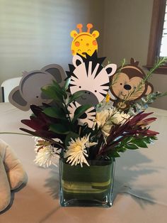 a vase filled with flowers and cut out animals sitting on top of a white table