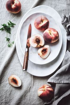 a white plate topped with sliced peaches next to a knife and fork on top of a table