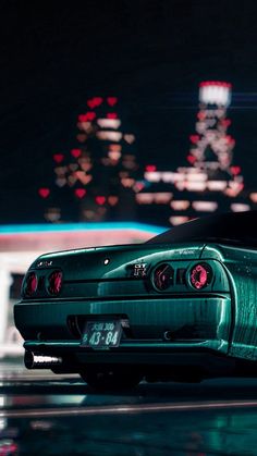 a green sports car parked in front of a building at night with city lights behind it