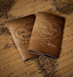 two personalized leather passport covers sitting on top of a world map with love is travel written on them