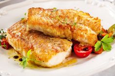 two fish fillets on a white plate with tomatoes and parsley sprigs