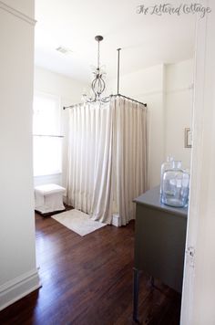 a white shower curtain in a bathroom next to a sink and toilet with wooden floors