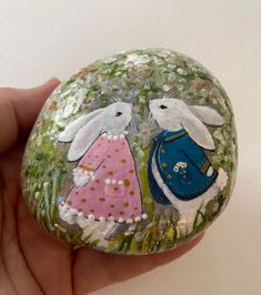 a hand holding a painted rock with two rabbits on it