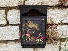 an old fashioned mailbox is decorated with flowers and fairy images on the side of a stone wall