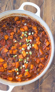 a pot filled with chili and sweet potatoes on top of a wooden table next to a spoon