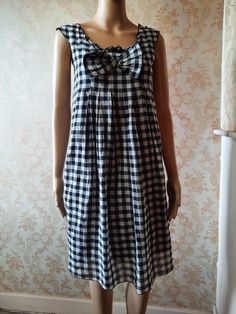 "Vintage smock style dress in black and white  gingham.  There is a small ruffle at the neck line and a large bow,  small pleats with the dress flaring from the bust.  It has no sleeves and is lined in black cotton. Bust;   32\" Length from shoulder;      35\"      Made by   MADAME A PARIS        100%  cotton" Casual Plaid A-line Dress, Summer A-line Plaid Dress, Vintage Cotton Mini Dress With Ruffles, Vintage Plaid Mini Dress For Summer, Gingham Dress For Summer Daywear, Chic Gingham Mini Dress With Ruffles, Spring Gingham Sundress With Ruffles, Gingham Dresses For Summer Daywear, Summer Gingham Dress With Ruffles