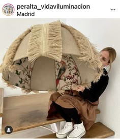 a woman sitting on top of a wooden bench next to an umbrella shaped like a bird