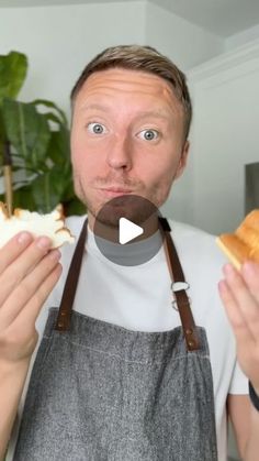 a man is holding food in one hand and looking at the camera while wearing an apron